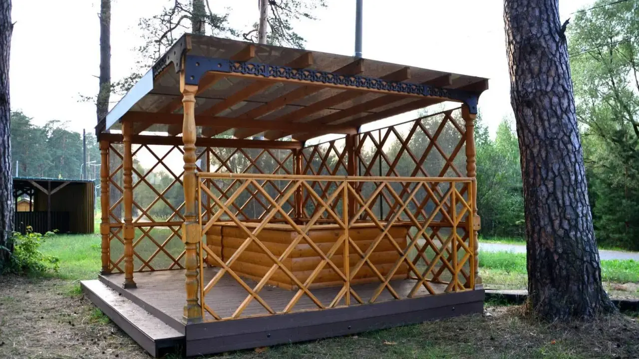 Drewniana altana z ażurową balustradą i przeszklonym dachem, stojąca na tarasie.