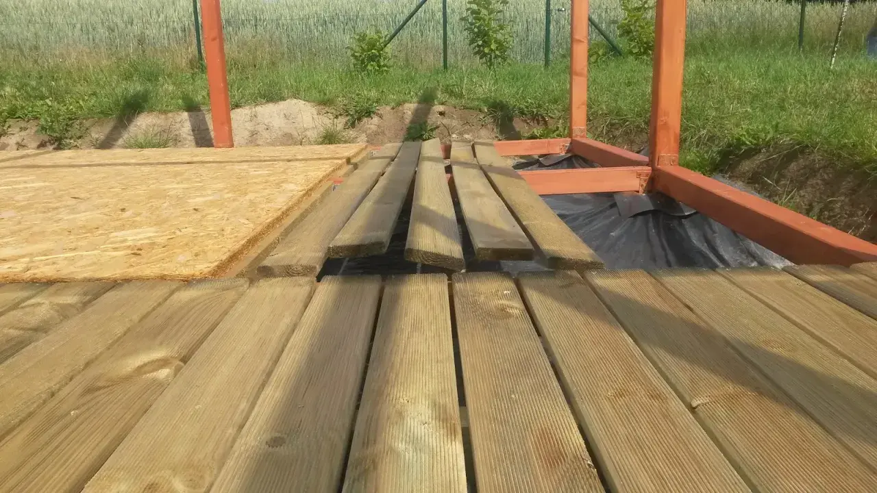 Drewniana konstrukcja altany w budowie, deski tarasowe i płyta OSB.