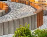 Betonowe słupki, z których można zrobić palisadę ogrodową, tworzą łuk wzdłuż ścieżki z kostki brukowej.