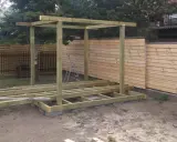 Konstrukcja altany w trakcie budowy. Drewniany szkielet i podłoga na bloczkach. W tle płot.