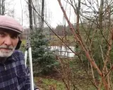 Mężczyzna z sekatorami pokazuje, jak przycinać morele. W tle widać drzewa i staw.