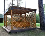 Drewniana altana z ażurową balustradą i przeszklonym dachem, stojąca na tarasie.