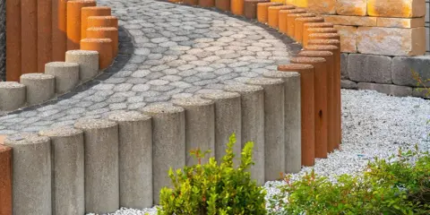 Betonowe słupki, z których można zrobić palisadę ogrodową, tworzą łuk wzdłuż ścieżki z kostki brukowej.