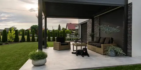 Nowoczesna pergola z zacienieniem, meble wypoczynkowe i pies. Idealne miejsce do relaksu, zastanawiasz się, czym zabezpieczyć pergole?