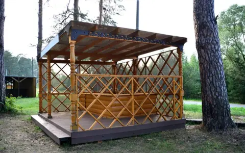 Drewniana altana z ażurową balustradą i przeszklonym dachem, stojąca na tarasie.