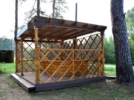 Drewniana altana z ażurową balustradą i przeszklonym dachem, stojąca na tarasie.