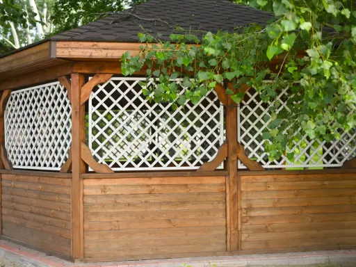 Drewniana altana z ażurowymi panelami i zielonymi liśćmi drzew.