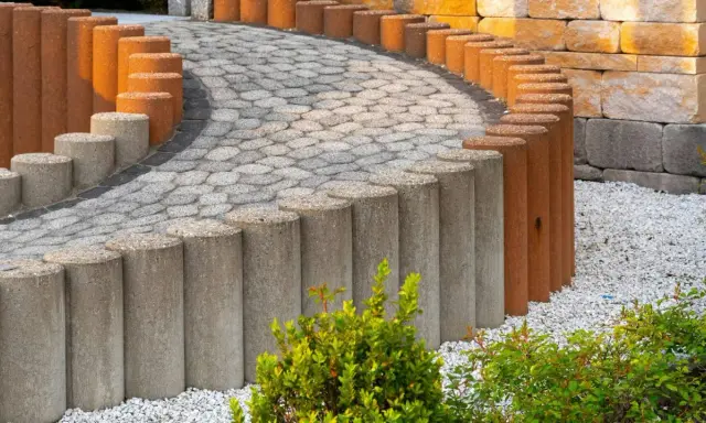 Betonowe słupki, z których można zrobić palisadę ogrodową, tworzą łuk wzdłuż ścieżki z kostki brukowej.