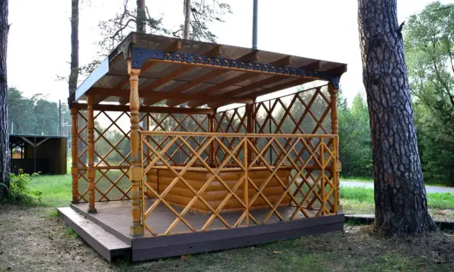 Drewniana altana z ażurową balustradą i przeszklonym dachem, stojąca na tarasie.