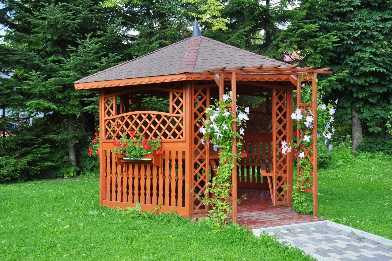 Drewniana altana w ogrodzie, ozdobiona kwiatami, zaprasza do odpoczynku. To idealne miejsce, by cieszyć się naturą.