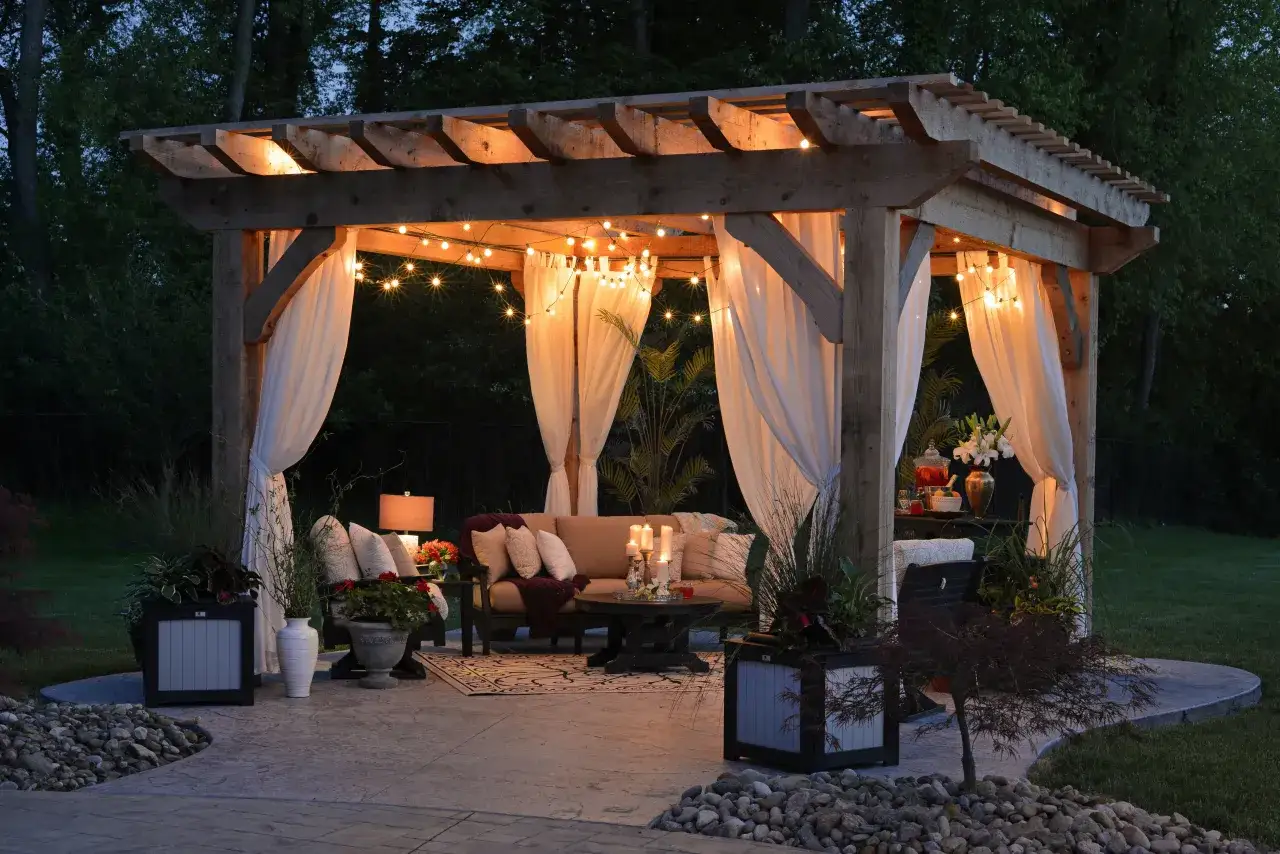 Przytulna pergola z oświetleniem i zasłonami, idealna na letnie wieczory. Wygodne meble i dekoracje tworzą magiczną atmosferę.