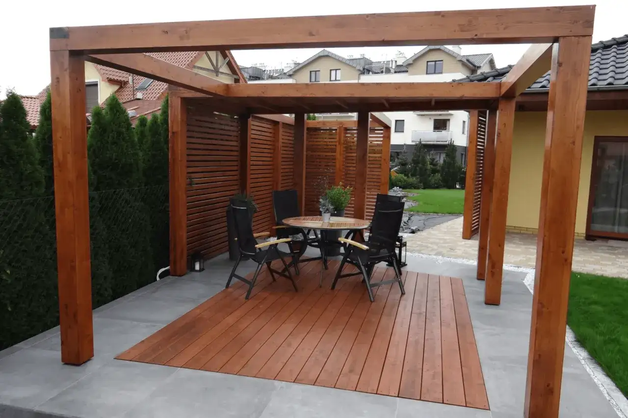 Drewniana pergola z miejscem do siedzenia i stołem, idealna na taras. Zastanawiasz się, co na pergolę w ogrodzie? Oto gotowe rozwiązanie!