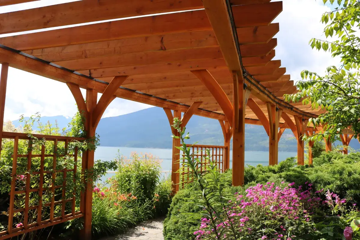Drewniana pergola nad jeziorem, z kwitnącymi kwiatami i zielenią. Inspiracja, jak zbudować pergolę.